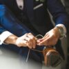 Close-up of a man in a suit tying his brown leather shoes, set indoors.