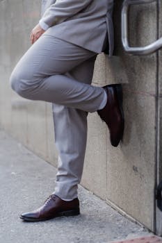 Partial view of man in formal attire leaning against an urban wall, with focus on shoes.